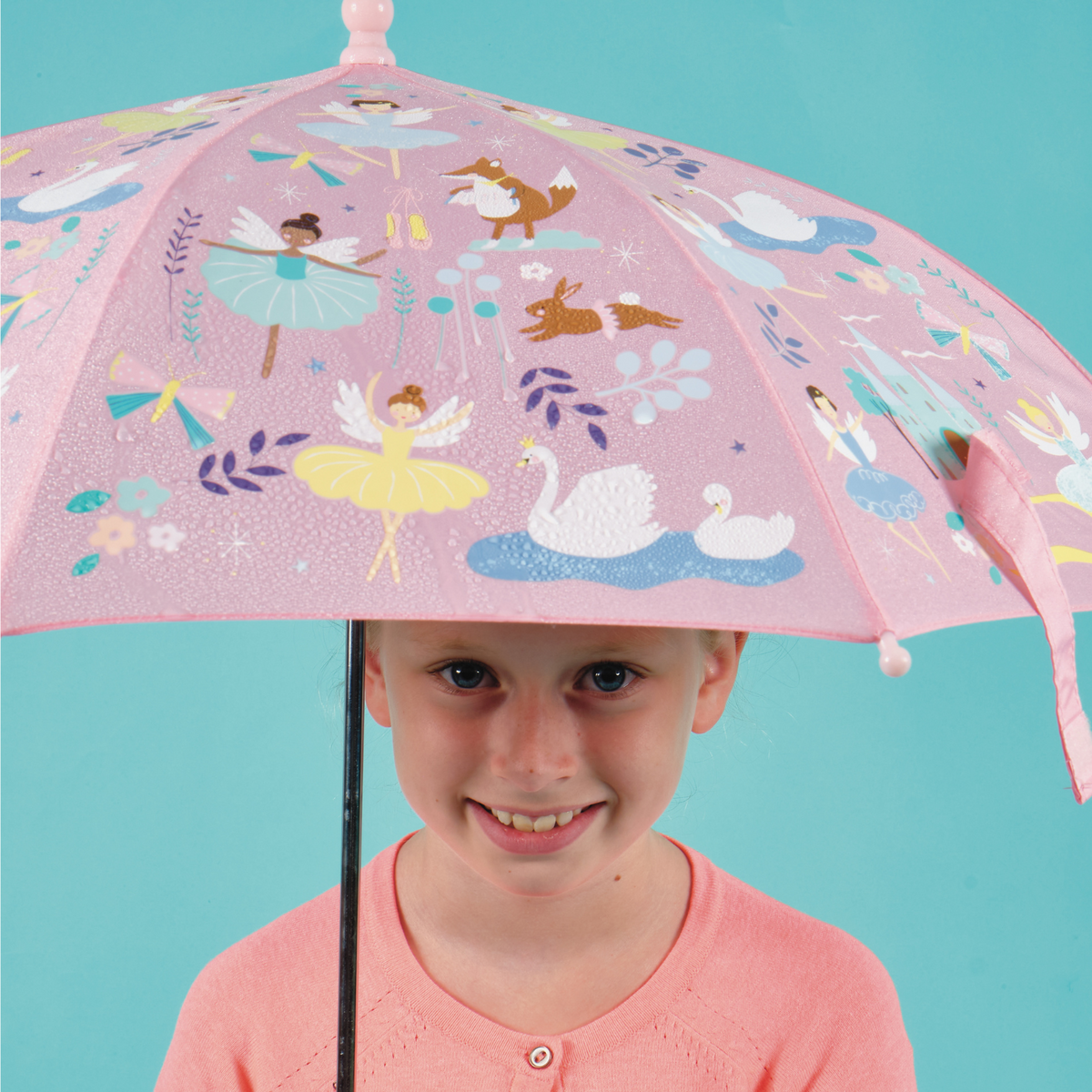 Girl holding A pink umbrella with various illustrations including ballet dancers and castles, designed for children.