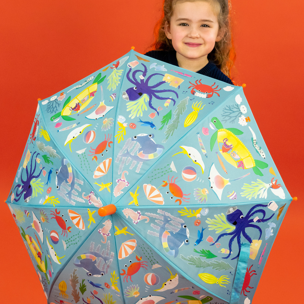 A girl holding the colour changing umbrella with a pattern of sea creatures including an octopus, turtle, and sharks displayed on a blue background.