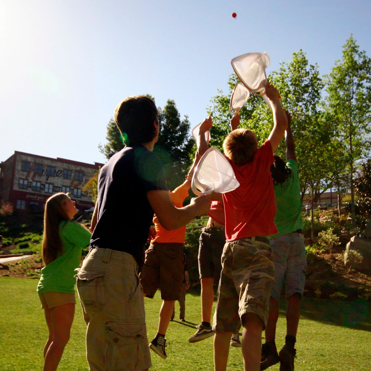 A group of friends playing Djubi Slingball on a sunny day, positioning the toy as a top choice for summer travel and holidays.