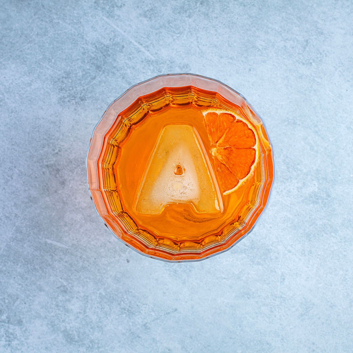 A single large ice letter A sitting in a crystal rocks glass with a dark spirit, showing how the personalised shape adds a sophisticated touch.