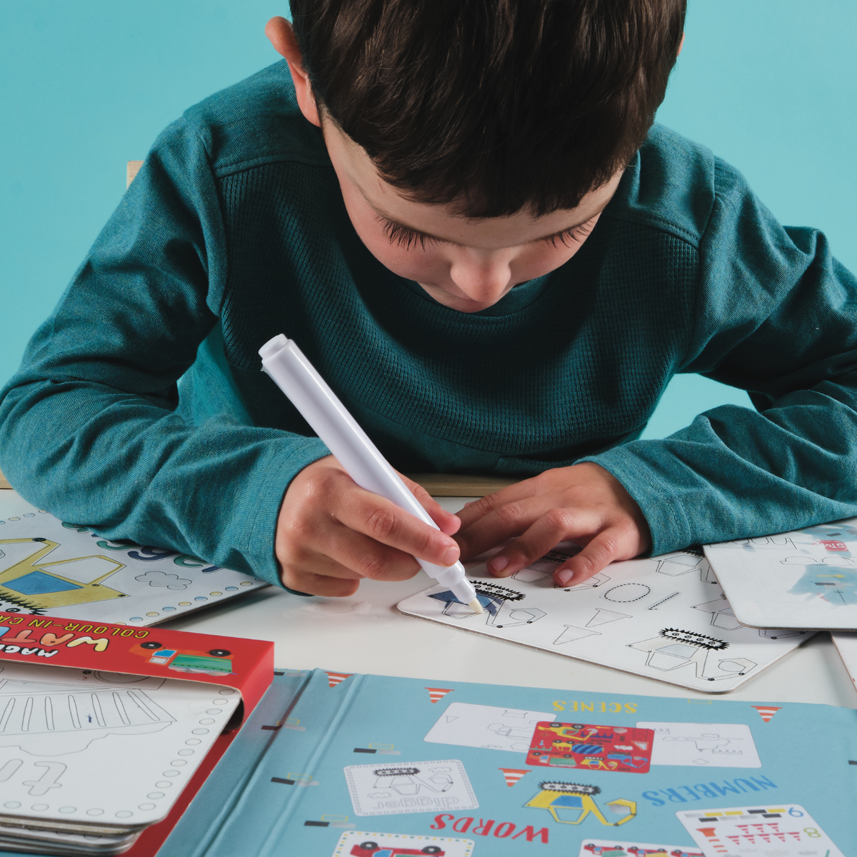 Boy sitting on table colouring in construction magic colour cards