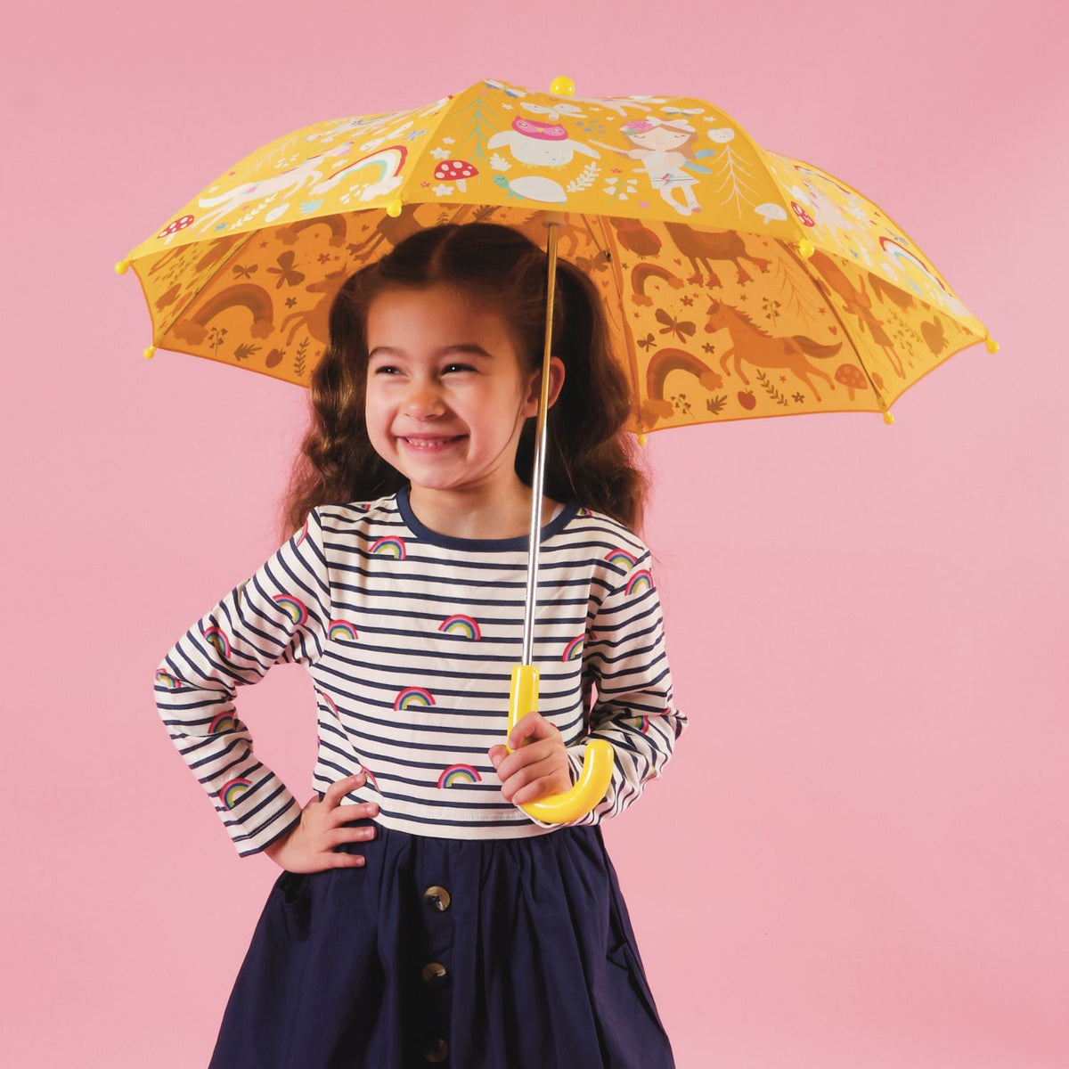 Child holding a yellow umbrella with rainbow fairy patterns