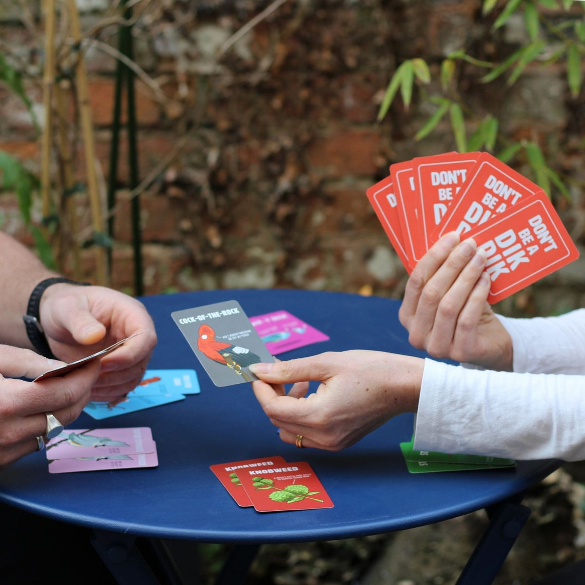 Two people playing a card game outdoors with colorful cards on a blue table.