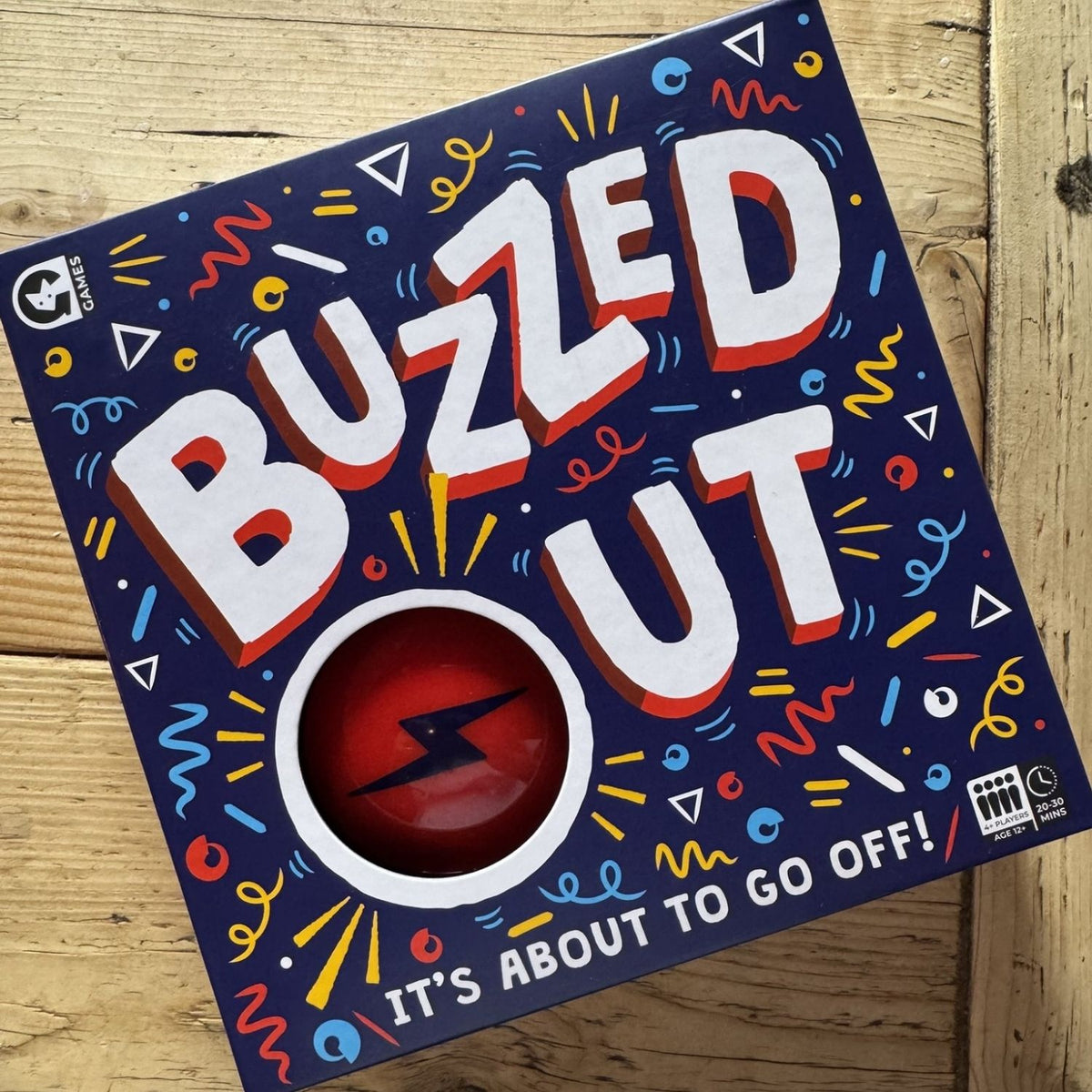 Board game box titled 'Buzzed Out' with colorful text and design on a wooden surface