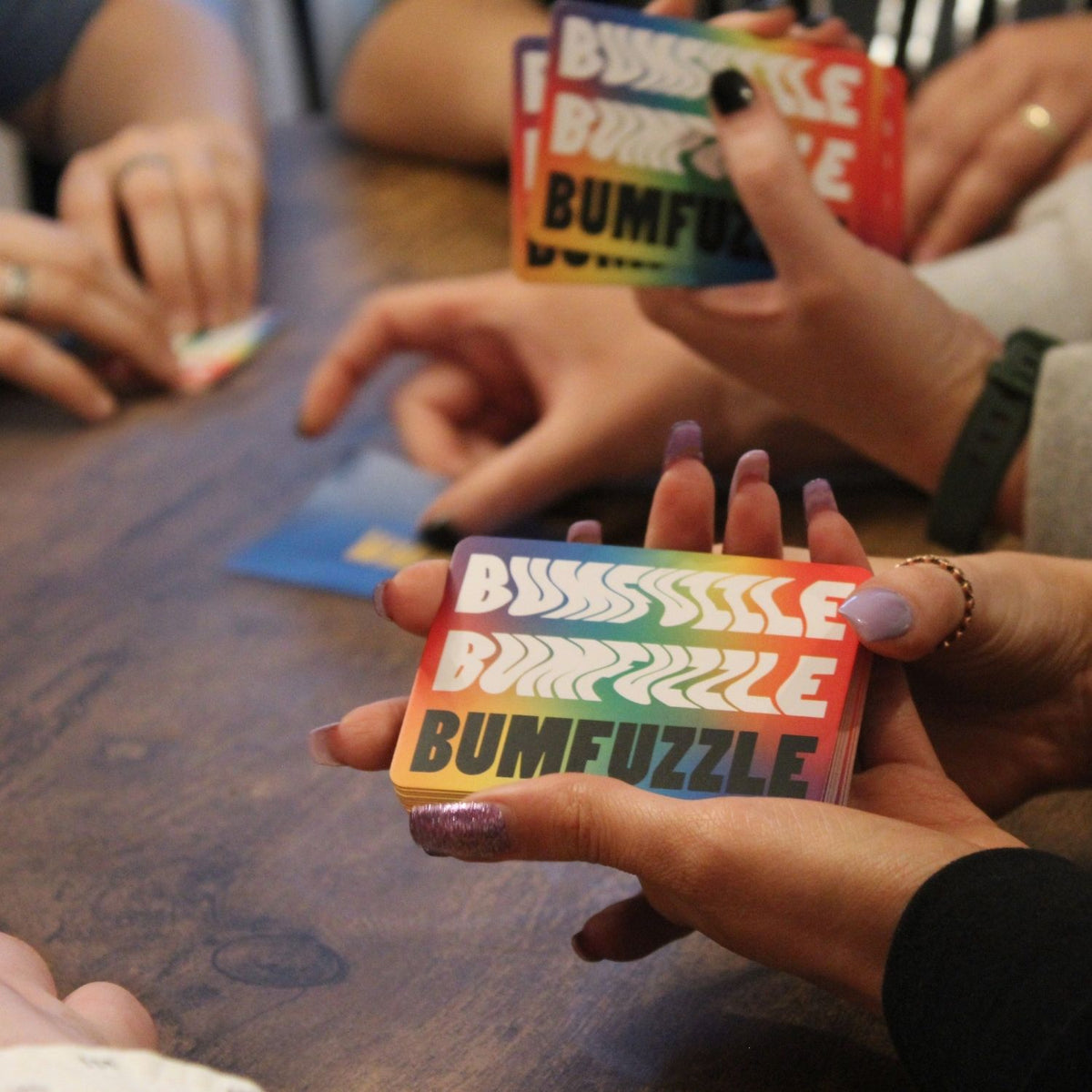 Hands holding colorful 'BUMFuzzle' cards on a wooden table
