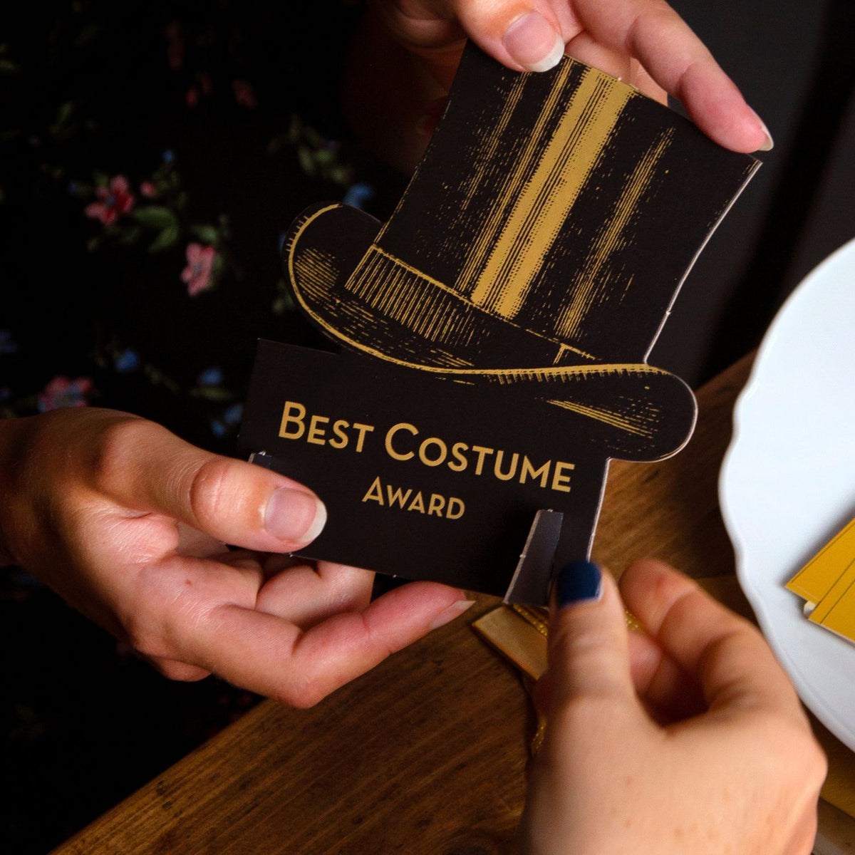 Person holding a 'Best Costume Award' card with a top hat design.