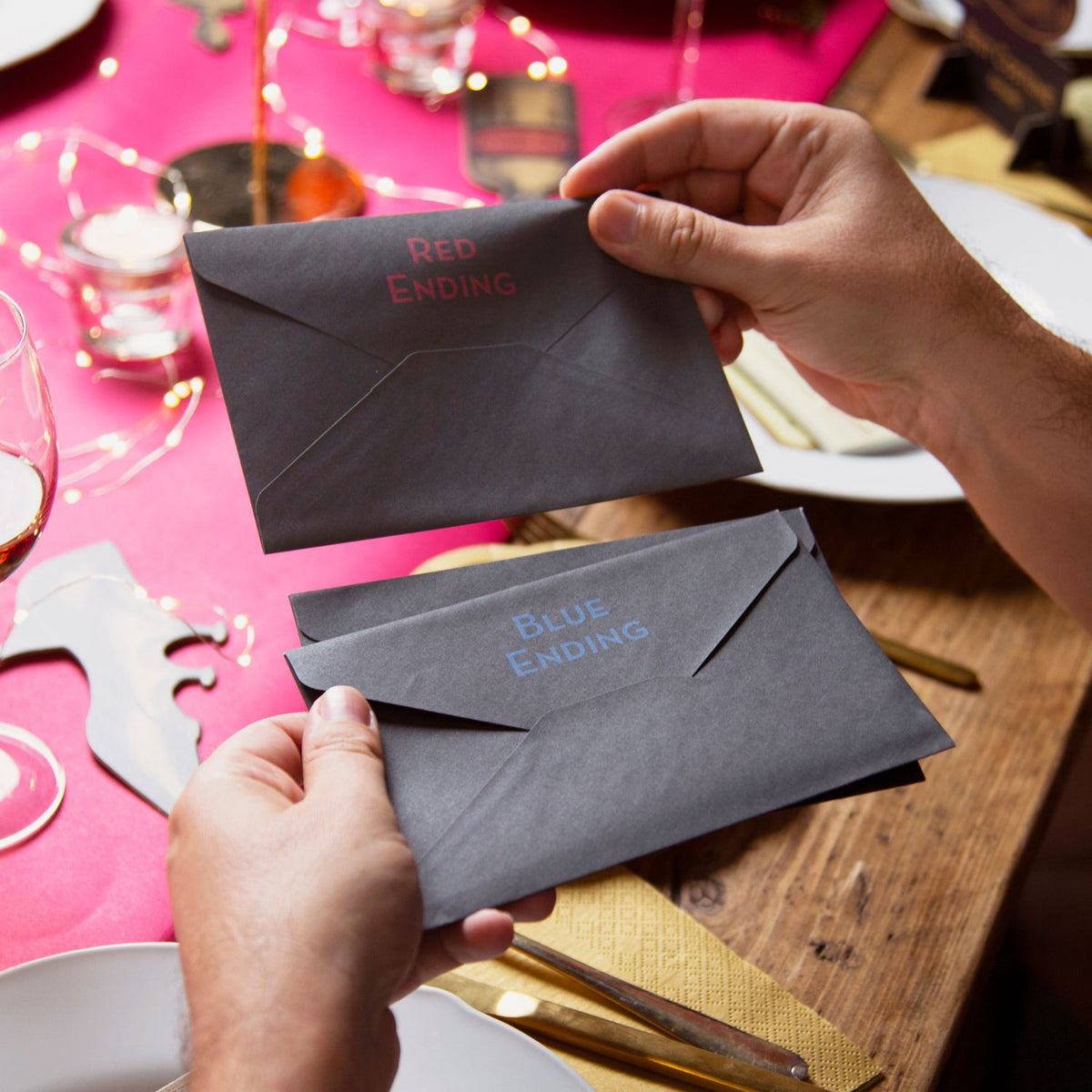 Two hands holding gray envelopes labeled 'Red Ending' and 'Blue Ending' on a festive table.