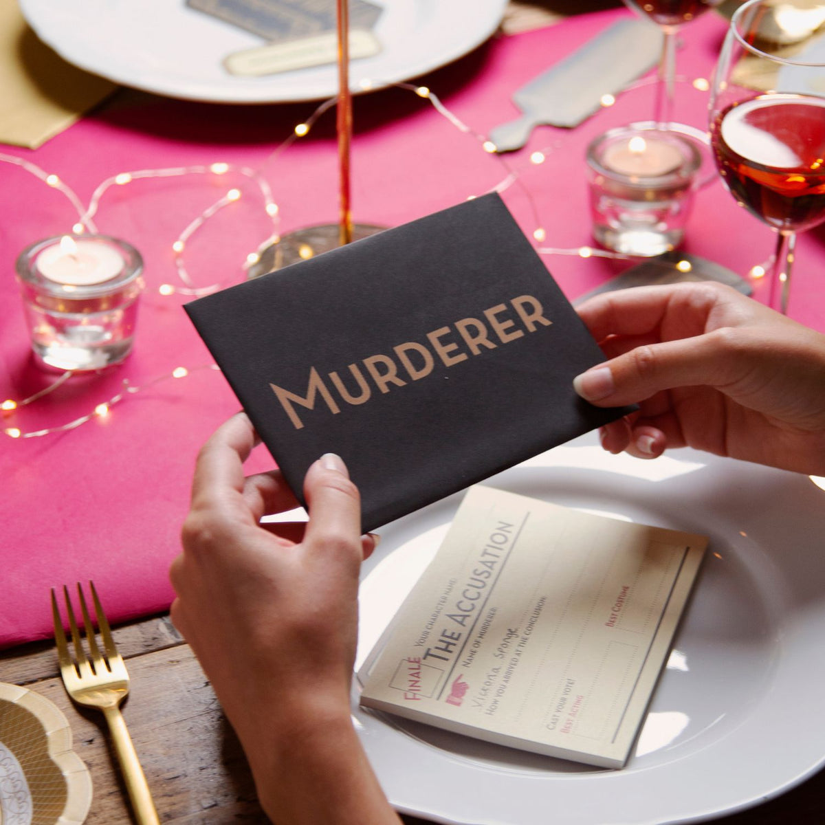 Person holding a book titled 'Murderer' on a table setting with candles and glasses.