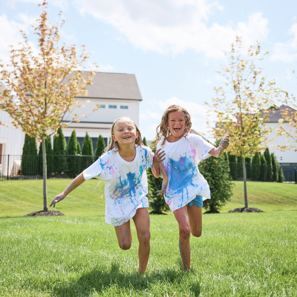 two girls running on grass with paint covered tshirts