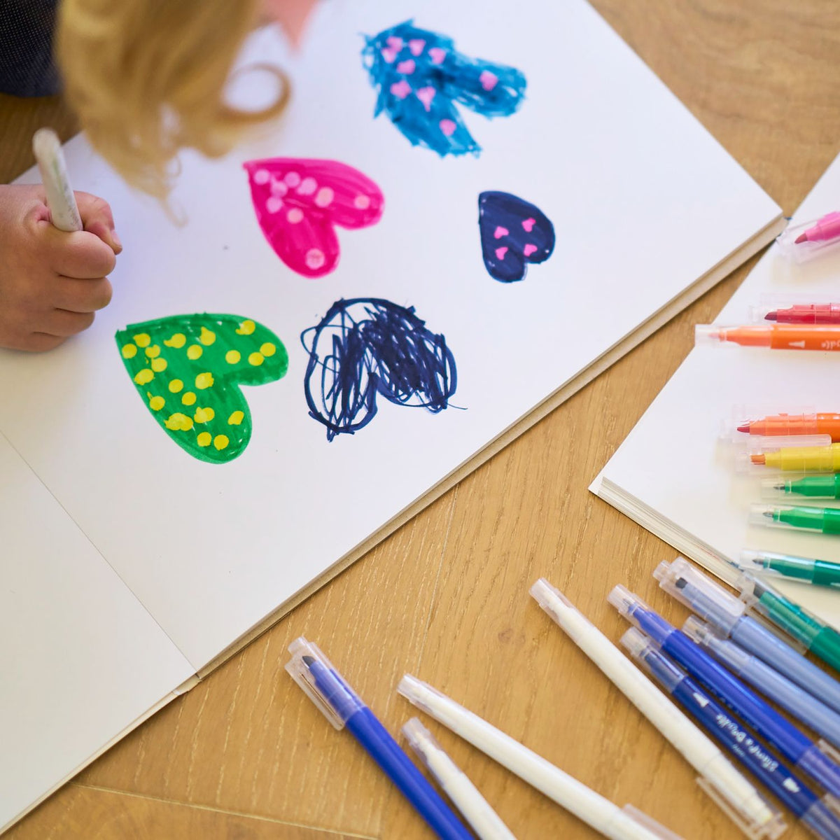 A child smiling while adding heart and circle patterns to a poster, showing the ease of use for small hands.