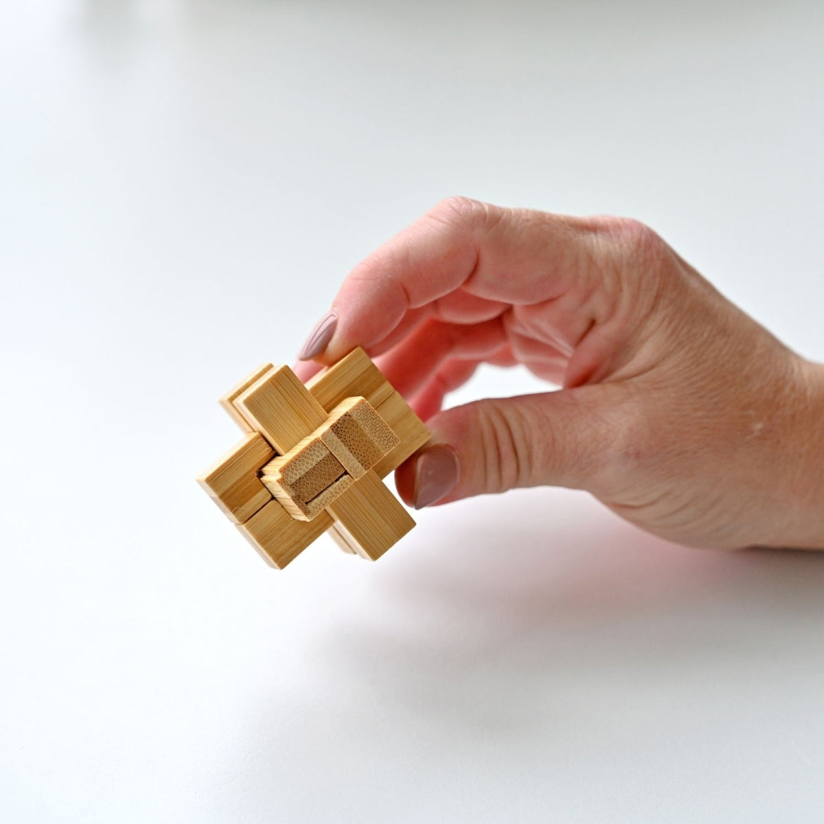 Hand holding a wooden interlocking puzzle against a white background