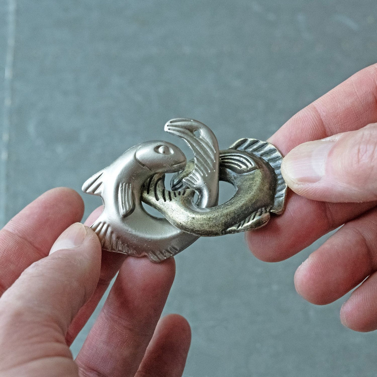 A close-up of a person’s hands meticulously manipulating the "Fish Fight" metal pieces to find the point of separation.