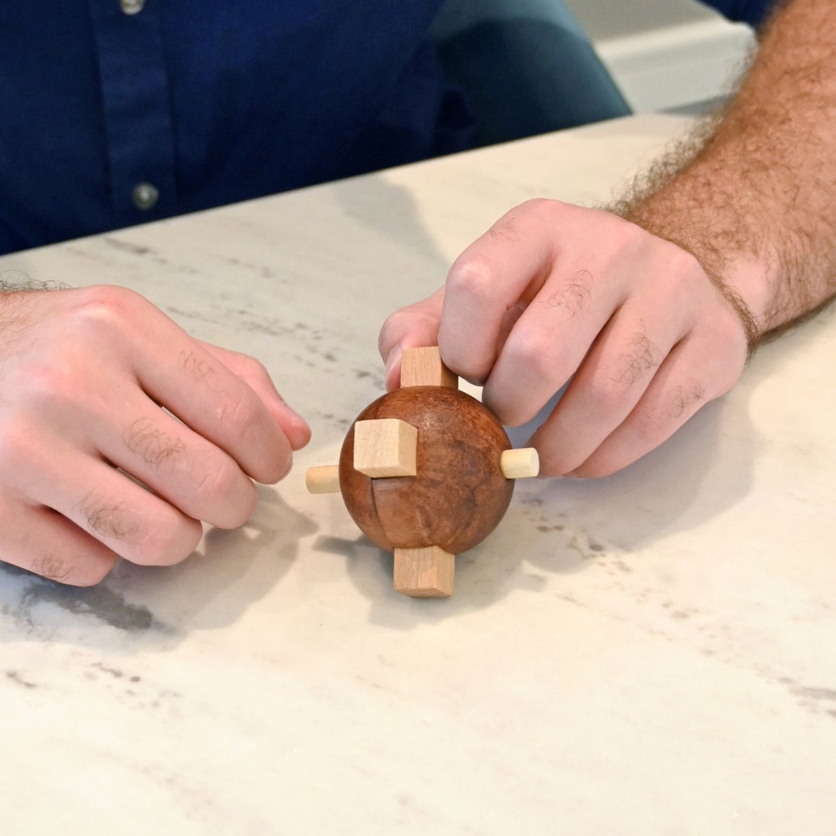 Person assembling a wooden puzzle. Attempting to disassemble the Egyptian Knot puzzle, highlighting the tactile wooden construction and mechanical challenge.