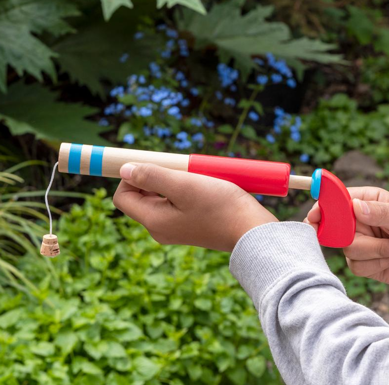 Child's hand holding a red and beige catapult with a small object attached, outdoors.