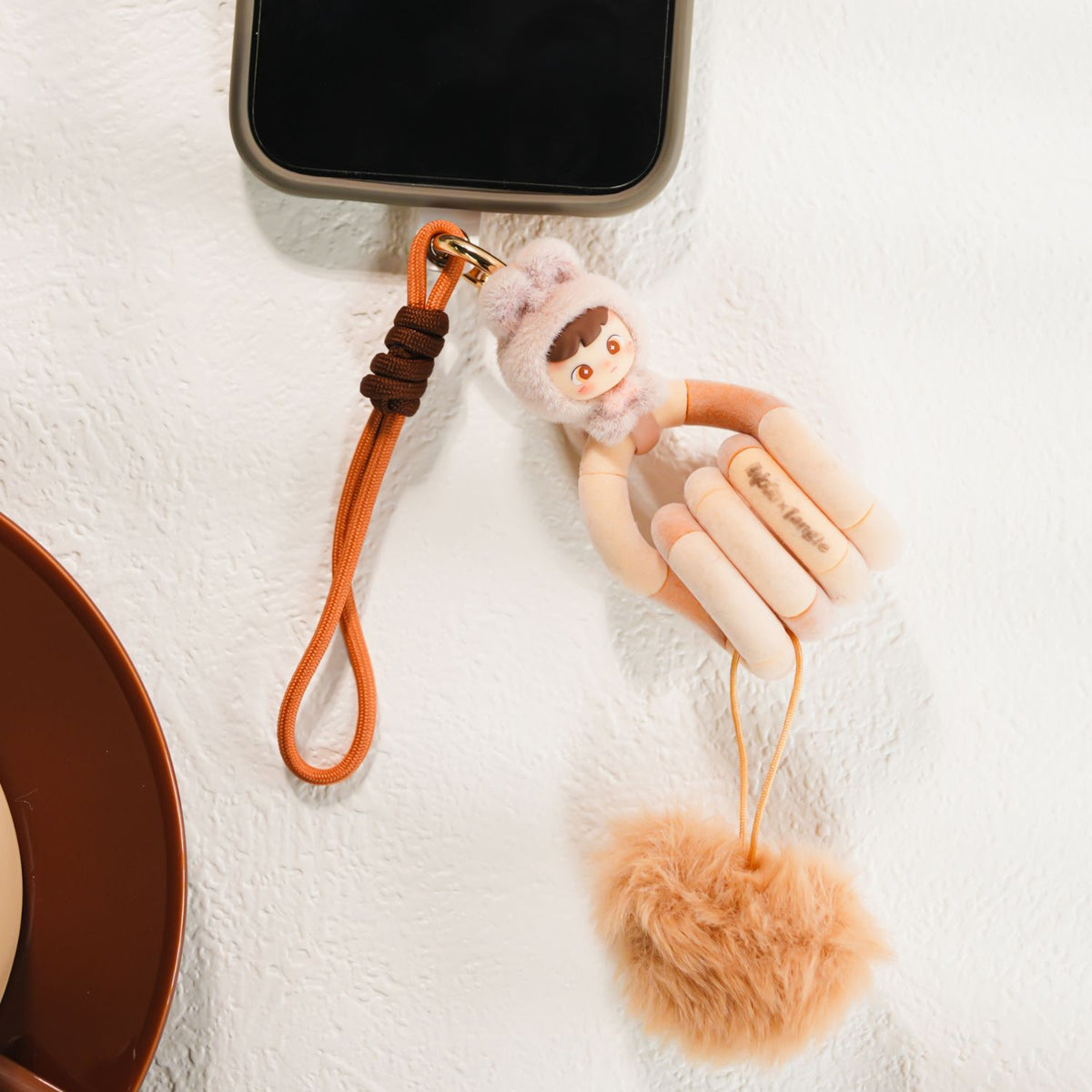 close-up product shot on a clean white background focusing on the Rare Beige sensory Tangle, twisted into a continuous loop to highlight its smooth, high-end neutral textured cream-beige segments and pom pom attached to a phone as a phone or bag charm.