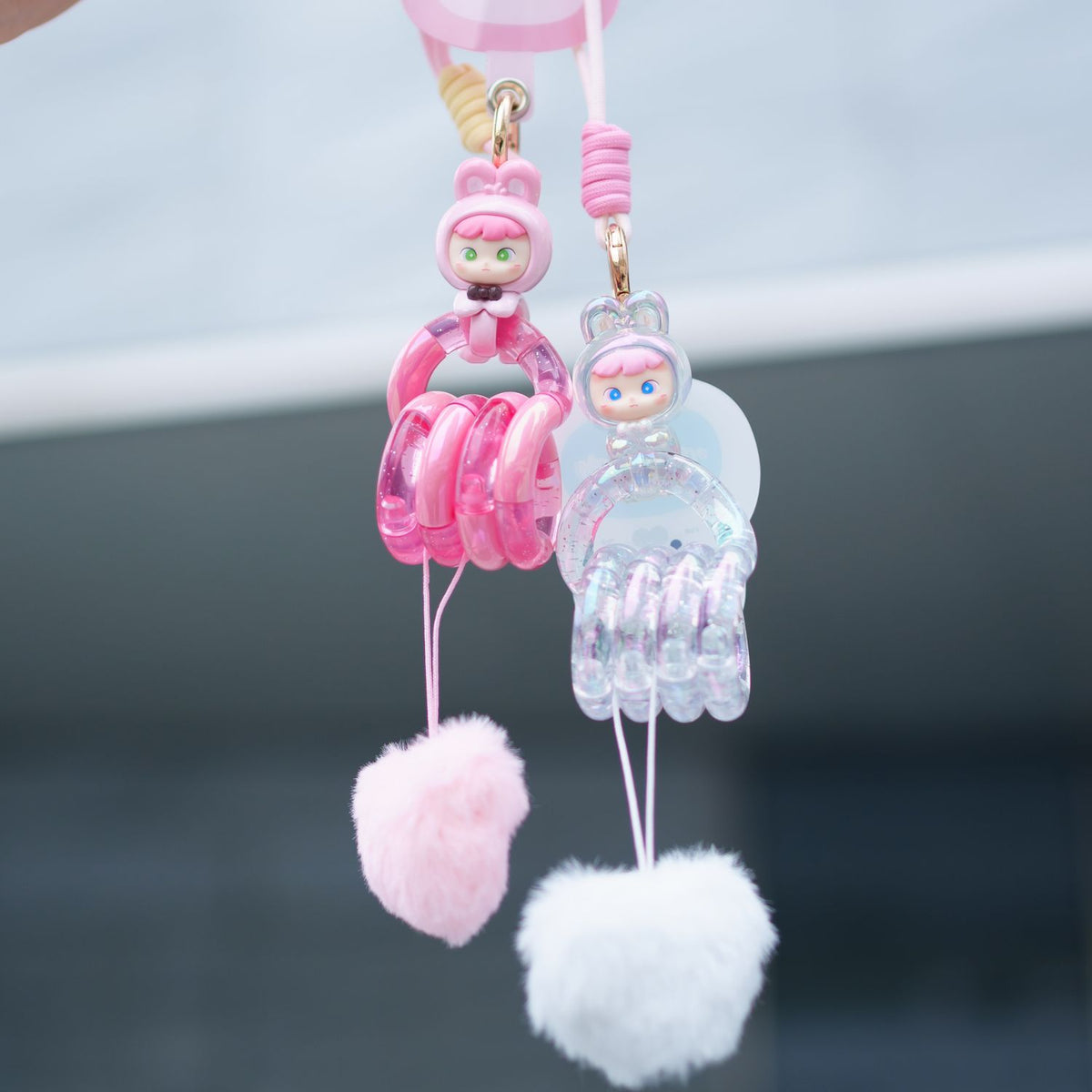 Pink and clear character keychains with fluffy poms on a blurred background